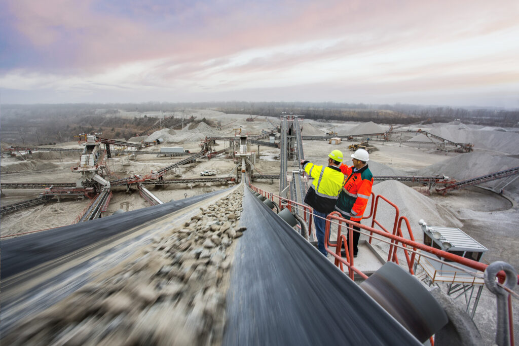 Workers at mine sitenext to conveyor belt with rocks